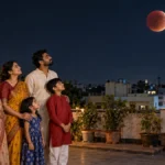 रात के समय अपने घर की छत पर खड़े होकर शांत मन से आसमान की ओर देखते हुए भारतीय परिवार के लोग।